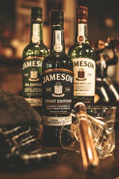 three bottles of jameson sitting on top of a wooden table next to a pair of glasses