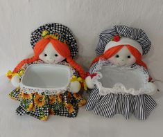 two dolls are sitting next to each other on a white surface and one is holding a mirror