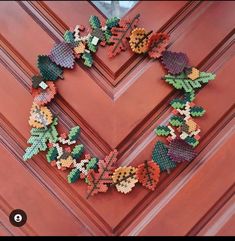 a heart shaped beaded wreath on a door with leaves and flowers in the center