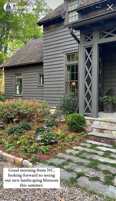 a gray house with stone steps leading to the front door and side porch, surrounded by greenery