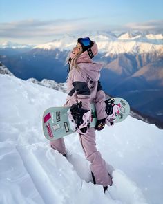 a woman standing on top of a snow covered slope with a snowboard in her hand