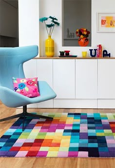 a brightly colored rug in the middle of a room with a blue chair and white cabinets