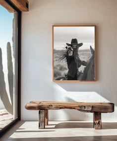 a black and white photo hangs on the wall next to a wooden bench in front of a window