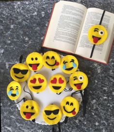 an open book sitting on top of a table next to cupcakes with faces