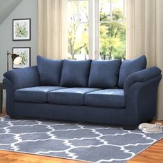 a blue couch sitting in front of a window on top of a wooden floor next to a rug