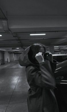 a woman standing next to a car talking on a cell phone in a parking garage