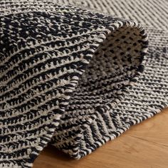 a black and white knitted blanket laying on top of a wooden floor with a hole in the middle