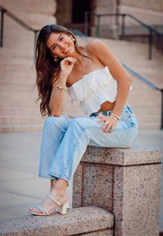 a beautiful woman sitting on top of a stone wall talking on a cell phone and smiling