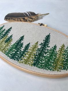 a hand embroidered wall hanging with pine trees on it and a feather in the background