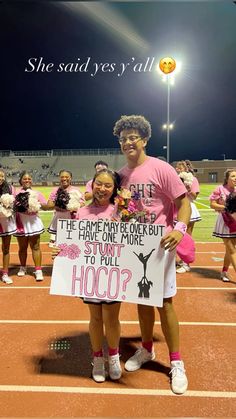 two girls are holding signs on the sidelines at a football game, and one girl is wearing a pink t - shirt that says she said yes y'all