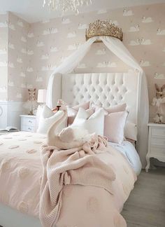 a bedroom with pink bedding and white headboard, chandelier and pillows