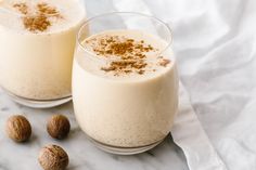 two glasses filled with milk and nuts on top of a white cloth next to each other