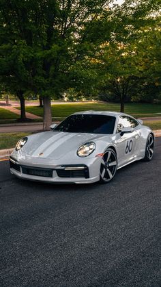 a silver sports car is parked on the side of the road in front of some trees