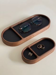 two wooden trays with sunglasses and rings in them on a white surface, one has a pair of glasses