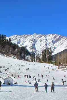 a group of people standing on top of a snow covered slope next to a mountain