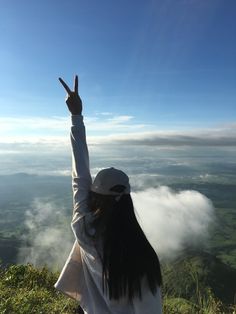 a woman standing on top of a lush green hillside with her hands in the air