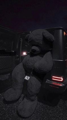 a large black teddy bear sitting on the back of a truck at night with its head down