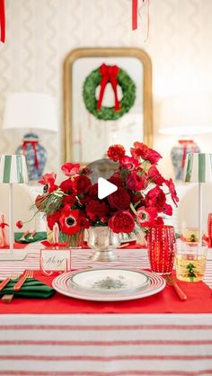 a table set for christmas with red flowers and greenery