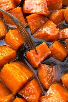 a fork is stuck into some cooked carrots in the pot with liquid on it