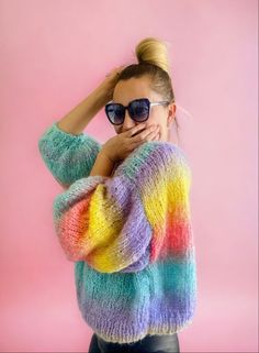 a woman wearing sunglasses and a colorful sweater poses for the camera with her hands on her head