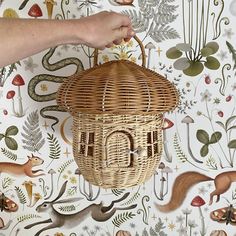 a hand is holding a wicker birdhouse in front of a floral wallpaper