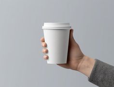 a person's hand holding a white coffee cup in front of a gray background