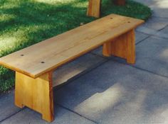 a wooden bench sitting on top of a cement ground next to green grass and trees