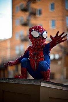 a stuffed spiderman is posed on the ledge in front of a building with its arms outstretched