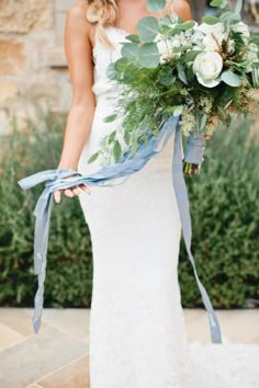 a woman in a white wedding dress holding a blue ribbon around her waist and bouquet