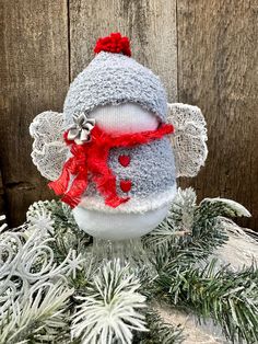 a knitted snowman ornament with red scarf and hat on top of pine branches