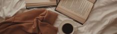 an open book and cup of coffee sit on a bed next to two opened books