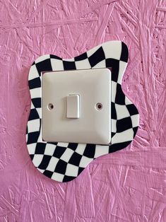 a black and white checkerboard light switch cover on a pink wall with a cat design