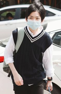 a young man wearing a face mask walks down the street in front of a car