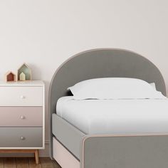 a white bed sitting next to a gray and pink dresser with a wooden night stand