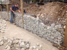 two men working on a fence made out of rocks