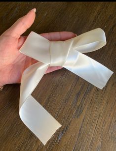 a person is holding a piece of white satin ribbon on top of a wooden table