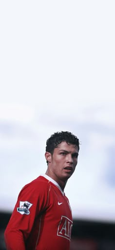 a young man in a red uniform standing on a soccer field with his head turned to the side