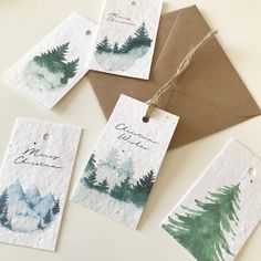 four tags with watercolor trees on them are hanging from a brown envelope and string