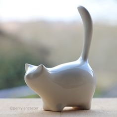 a white ceramic cat figurine sitting on top of a wooden table next to a window