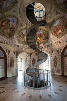 a spiral staircase in an ornate building with paintings on the walls