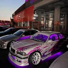 several cars parked in front of a building with purple lighting on the hood and sides