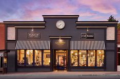 a store front with a clock mounted on the side of it's building at dusk