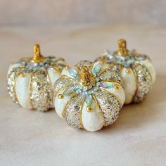 two white pumpkins with gold glitter decorations on them