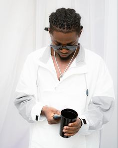 a man in white shirt and sunglasses holding a black cup while looking at his cell phone