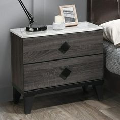 a night stand with two drawers and a lamp next to it on top of a bed