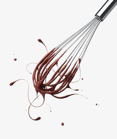 a whisk filled with chocolate sauce on top of a white table next to spilled chocolate