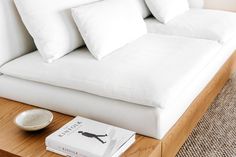 a white couch with pillows and a book on the coffee table in front of it