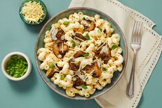 a bowl filled with pasta and mushrooms next to a small bowl of green peas on a napkin