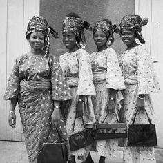 an old photo of four women in african dress and head scarves standing next to each other