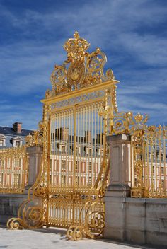 an ornate golden gate in front of a building with blue sky and clouds behind it